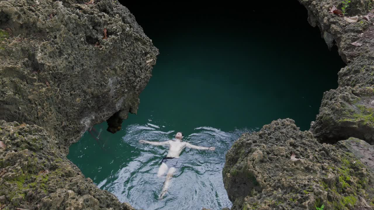 游泳者漂浮在菲律宾卡巴尼奥池洞清澈的海水中，周围是崎岖的悬崖视频素材