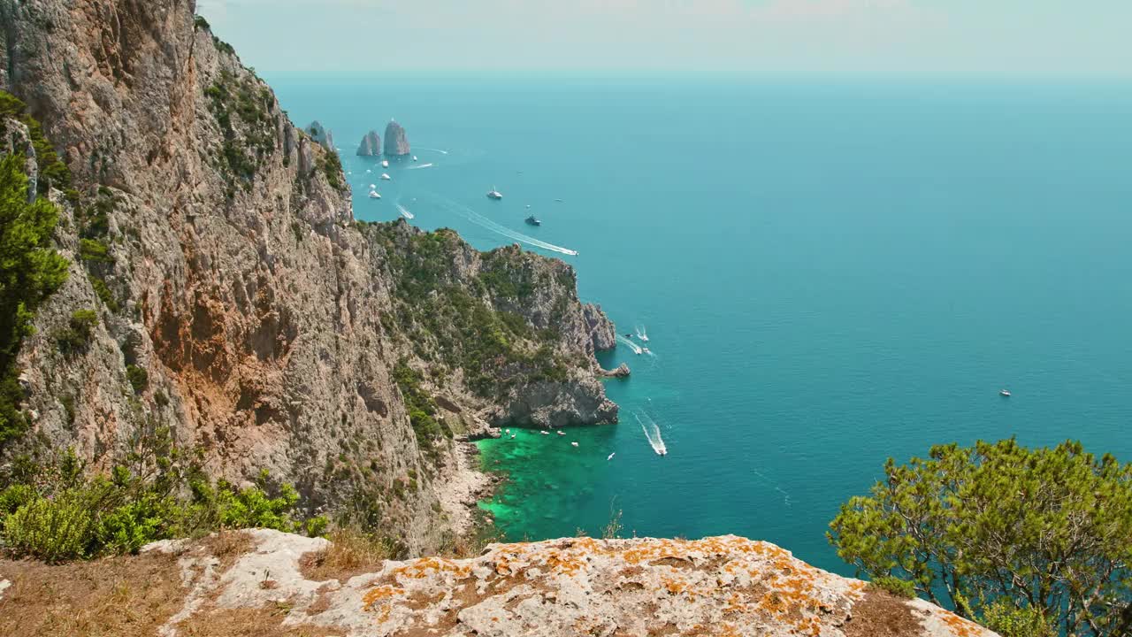 在温暖的夏季，沿着卡普里岛的高悬崖徒步旅行，俯瞰清澈蔚蓝的大海，到处都是船只。Faraglioni堆叠在背景上。视频素材