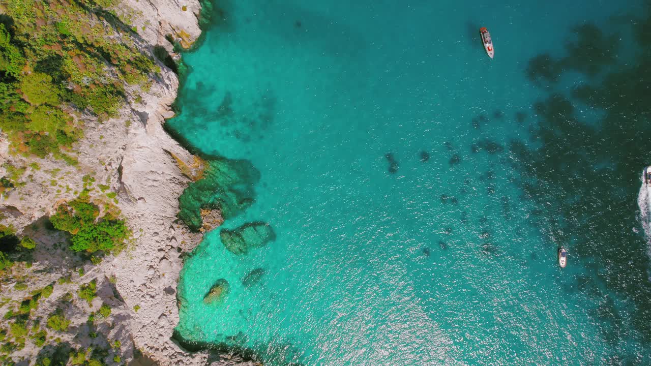 一个令人惊叹的自上而下的观点，船只漂浮在清澈的绿松石海水附近崎岖的悬崖。意大利卡普里岛。视频素材