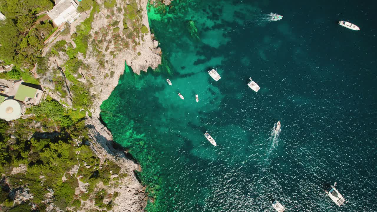 海岸空中景观与船和岩石悬崖在夏季郁郁葱葱的绿色植物。标志性的海蚀柱法拉格列尼出现在意大利卡普里岛蔚蓝的海水中。视频素材