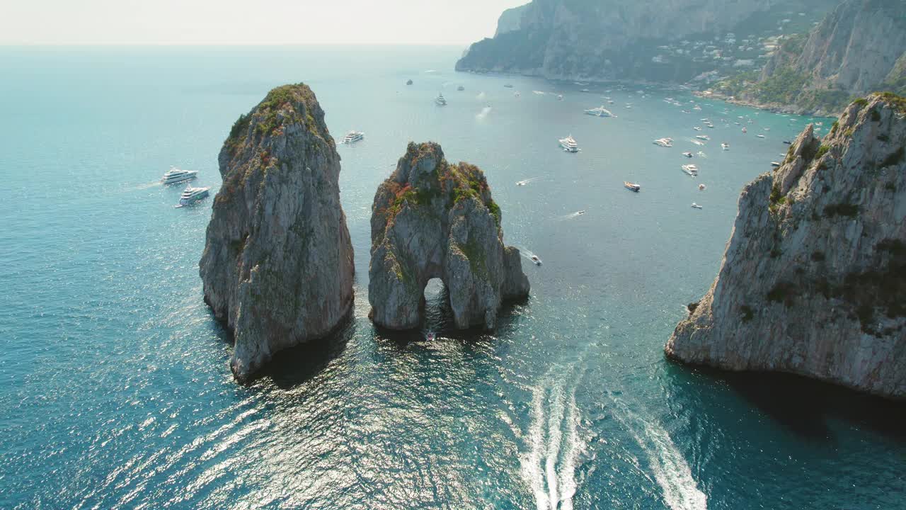 雄伟的海蚀柱从意大利卡普里岛的蓝色海水中升起。船只漂浮在第勒尼安海的天然岩层周围。视频素材