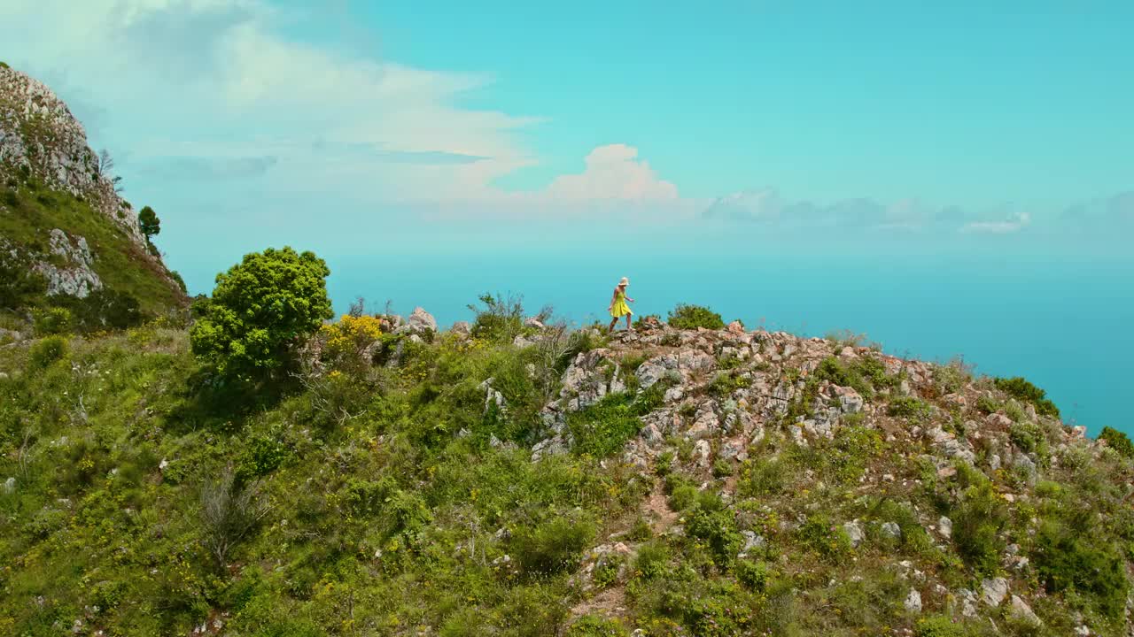 从落基山顶眺望大海的独自旅行者。一个孤独的女人沿着海岸线走着，俯瞰着蔚蓝的大海和天空。意大利卡普里岛。视频素材