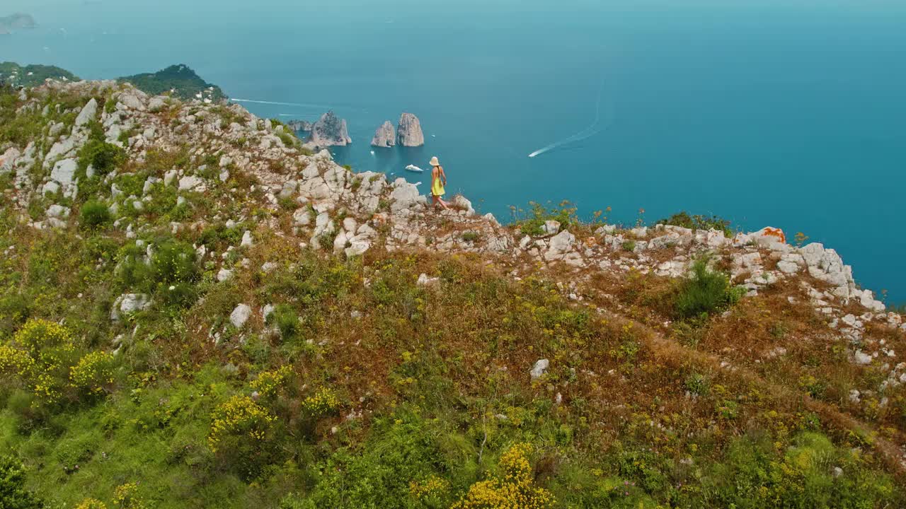 身穿夏装的女子欣赏海岸美景。游客从高处欣赏大海、法拉格里奥尼悬崖和船只的景色。意大利卡普里岛。视频素材