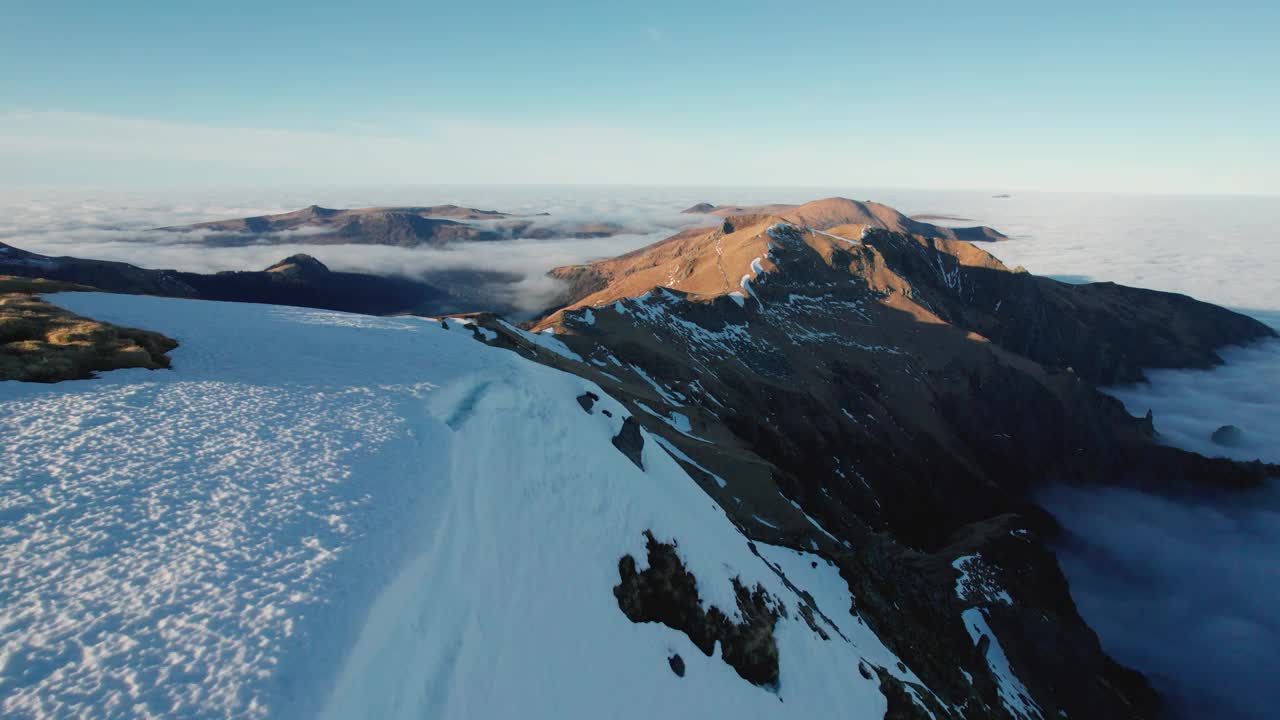 在法国中央奥弗涅火山国家公园，日落时分，山峰突出在云逆温之上。雪堆分布在山坡上。视频素材