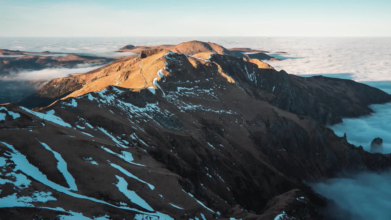 在法国奥弗涅中部火山国家公园的云层逆温期间，山峰的时间推移，山坡上有积雪，出现在云层之上。视频素材