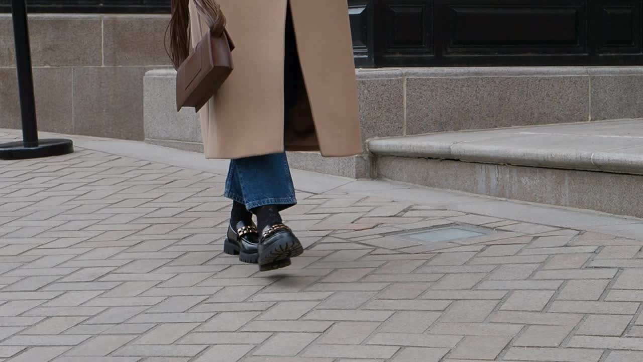 走在街上的女人穿着时髦的春秋季服装，羊绒外套，牛仔裤，黑色的乐福鞋和手提包。运动中的女模特，街头风格的时尚，近距离的腿视频下载