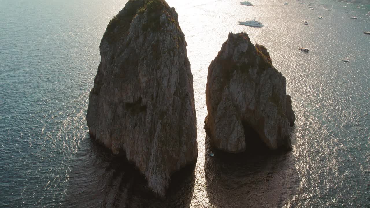 阳光散落在海面上的岩石峭壁周围，远处有船只。黄昏时的鸟瞰图。视频素材