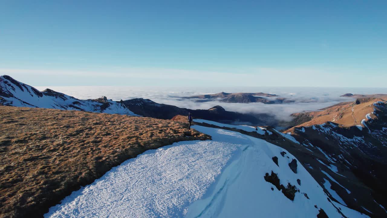 在法国中央奥弗涅火山国家公园，一个人站在山脊上，周围是雪和云。视频素材