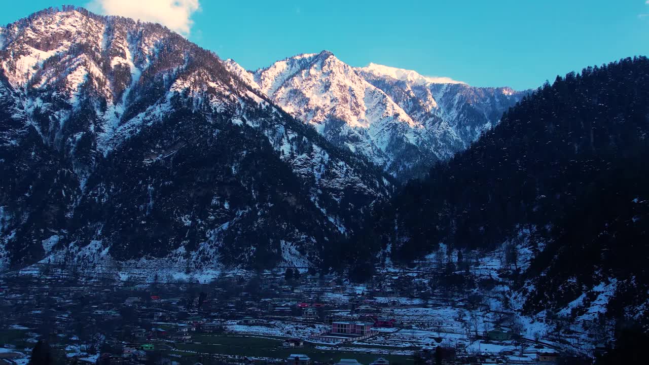 阳光普照的白雪皑皑的山峰俯视着有村庄的山谷视频素材