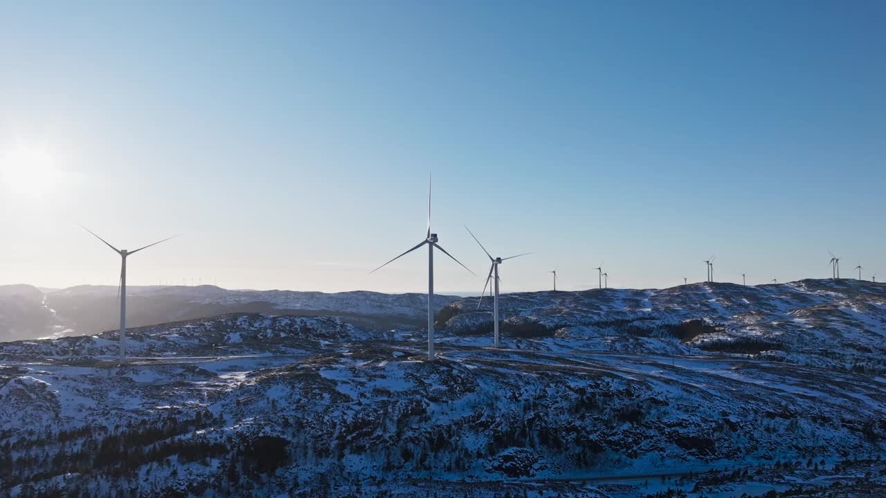 日出时白雪覆盖的土地上一动不动的风力涡轮机。挪威的Bessakerfjellet风电场。无人机拍摄的视频素材