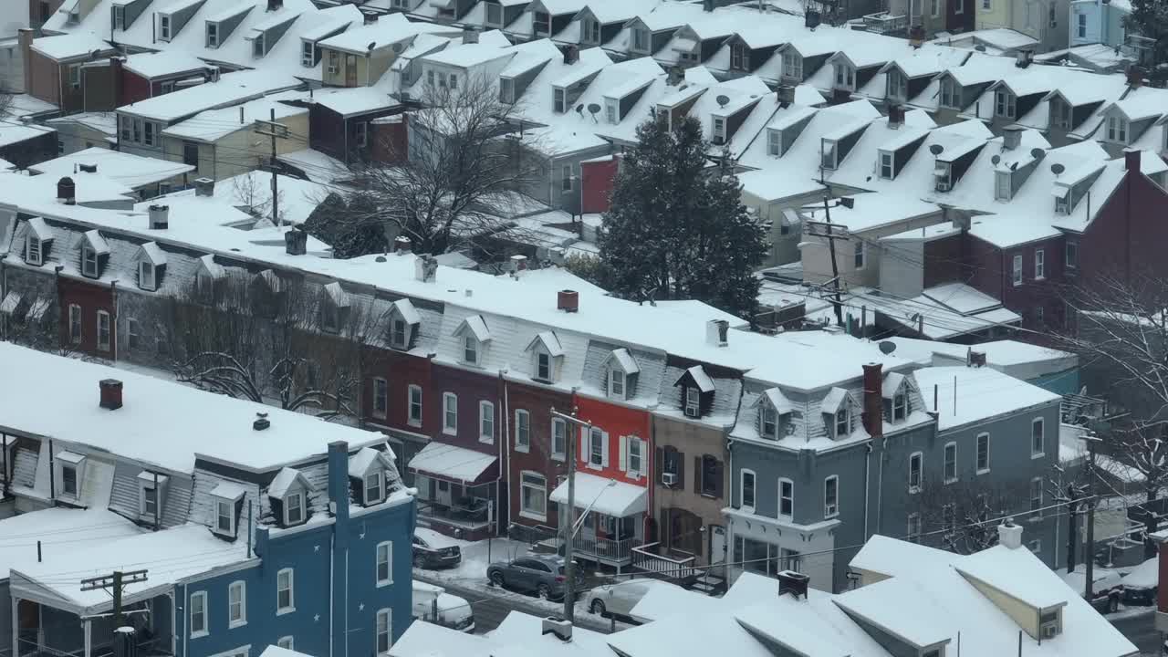 在美国下雪的冬日里，美丽拥挤的一排排房屋有着五颜六色的外墙。雪中的房屋和家园。空中倾斜向上变焦镜头。视频素材