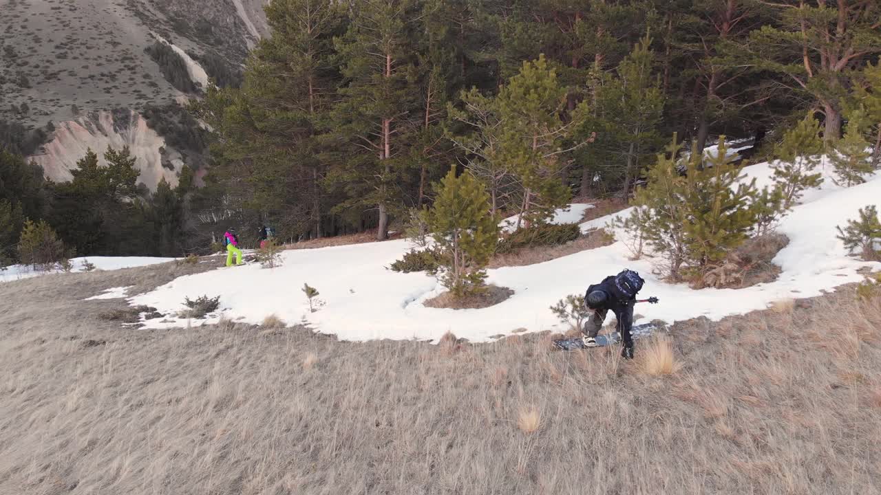 鸟瞰图女运动员公司在滑雪板和滑雪板上走下雪坡在春天。最后的自由骑行，穷乡僻岭。在干草地上高山滑雪视频素材