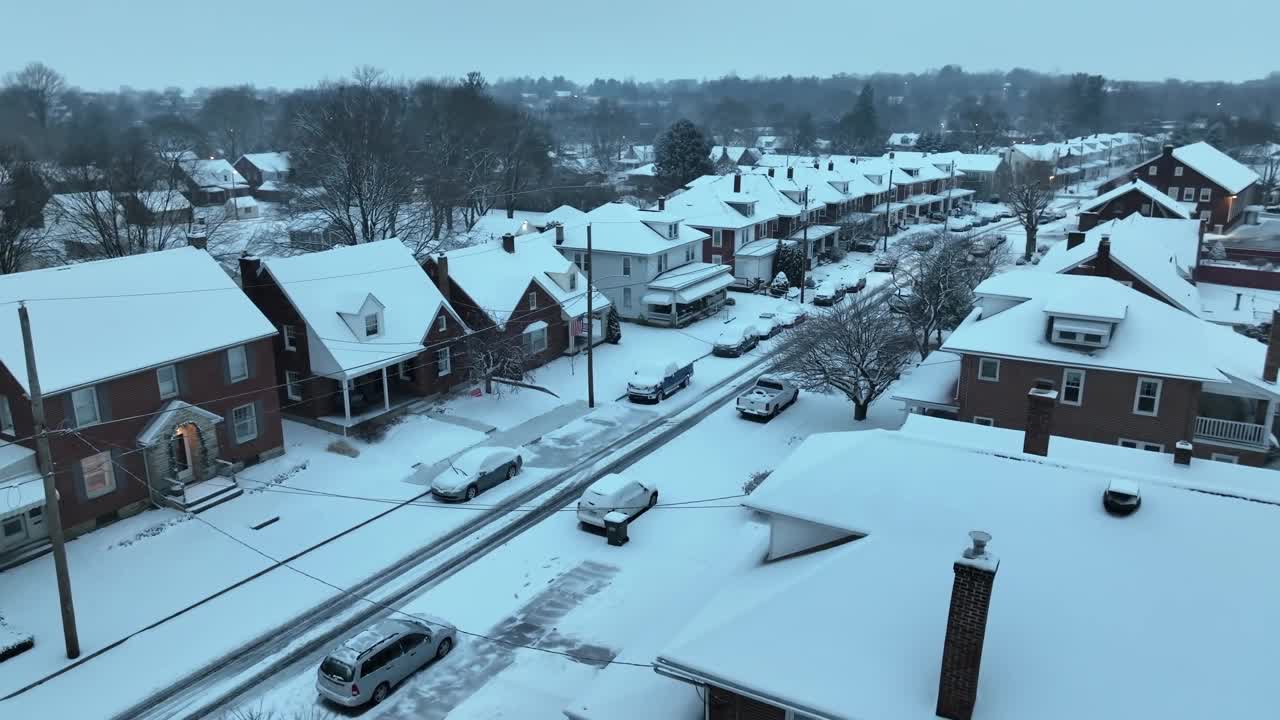 白雪皑皑的住宅区，砖房和停着的汽车，背景是树木。冬季在美国城镇的航拍。视频素材