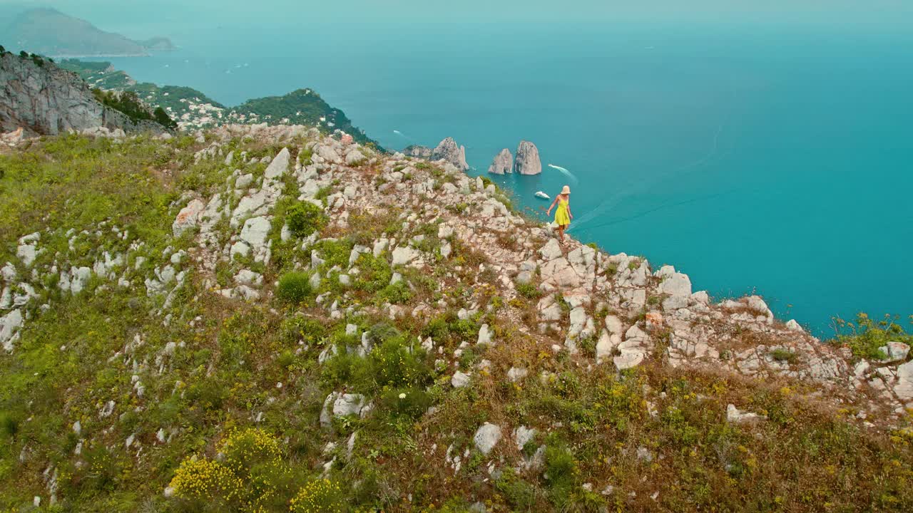 身穿夏装的女子在群山中徒步旅行，与卡普里岛的美景相伴，俯瞰蔚蓝的大海。著名的三个悬崖法拉格里奥尼为背景。视频素材