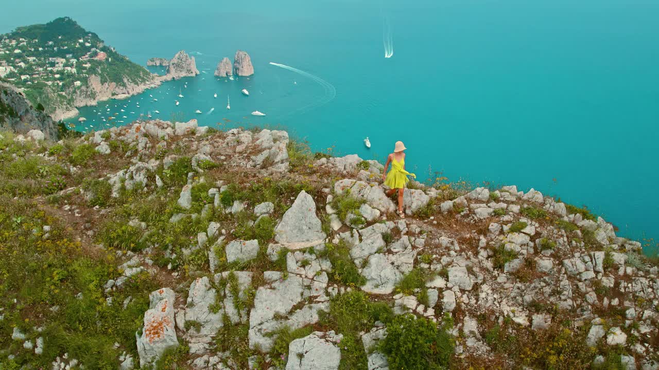 一名女子沿着山脊徒步旅行，欣赏着令人惊叹的海景。俯瞰意大利卡普里岛宁静的蓝色海水和岩石海岸。视频素材