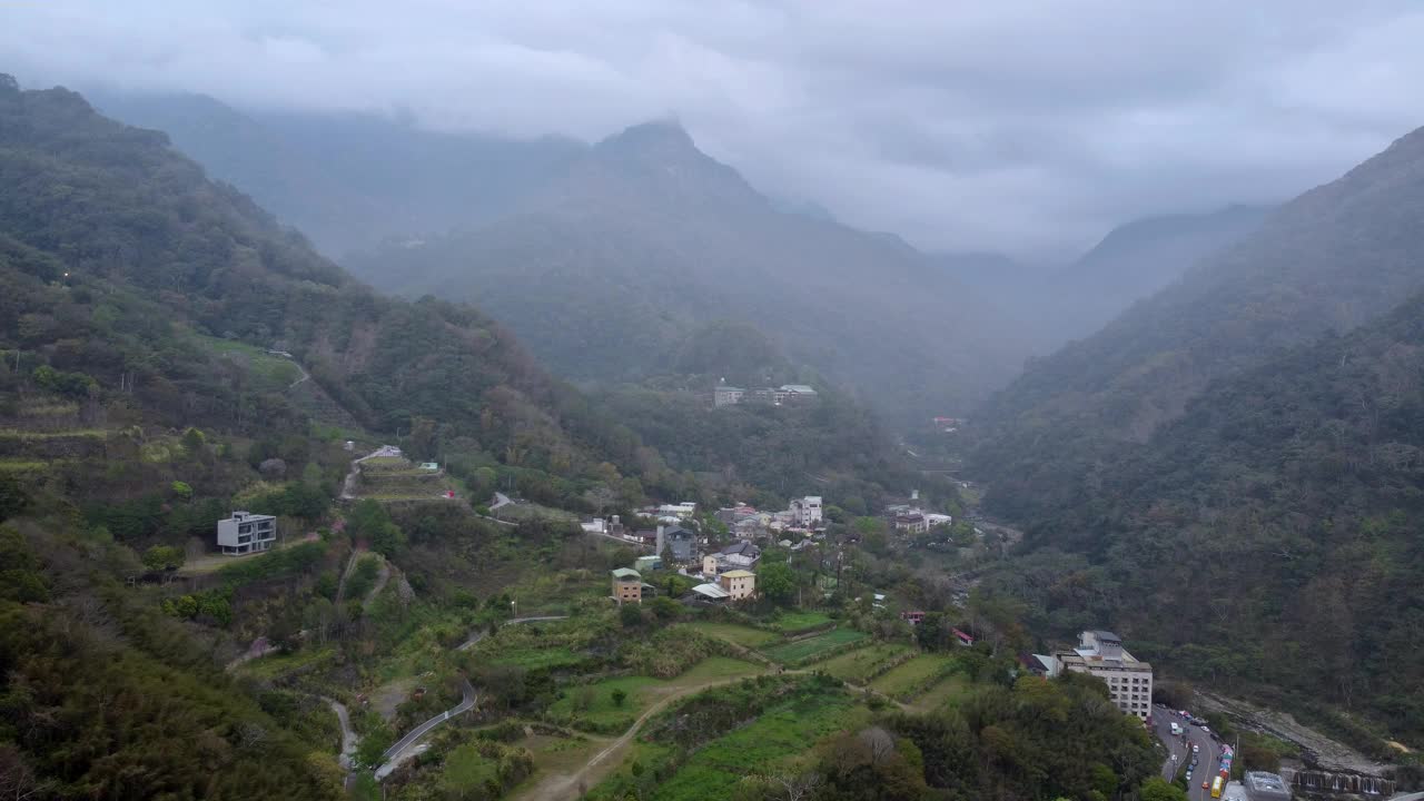 雾蒙蒙的山村坐落在郁郁葱葱的山谷中，阴天，鸟瞰视频素材