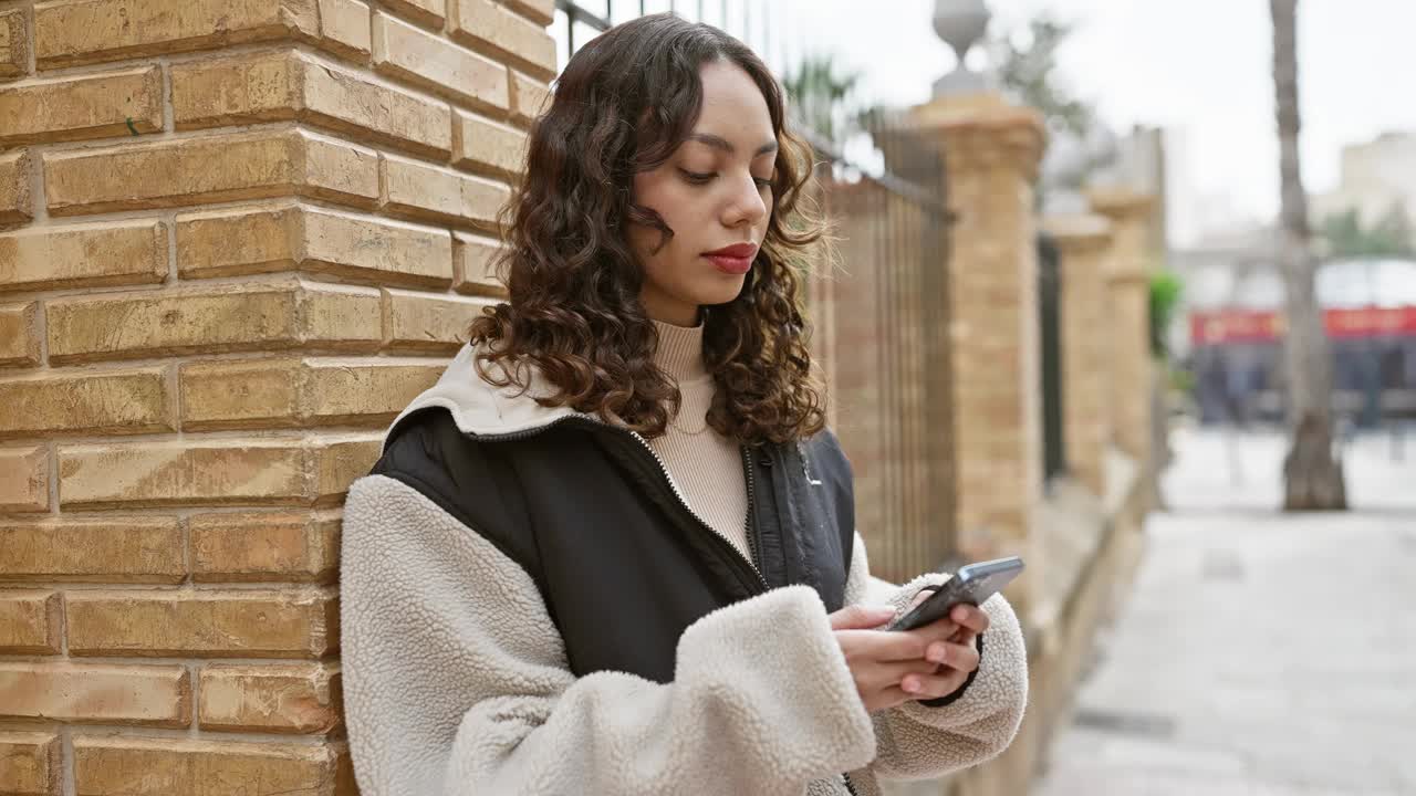 一名女子在城市街道上对着砖墙使用智能手机。视频素材