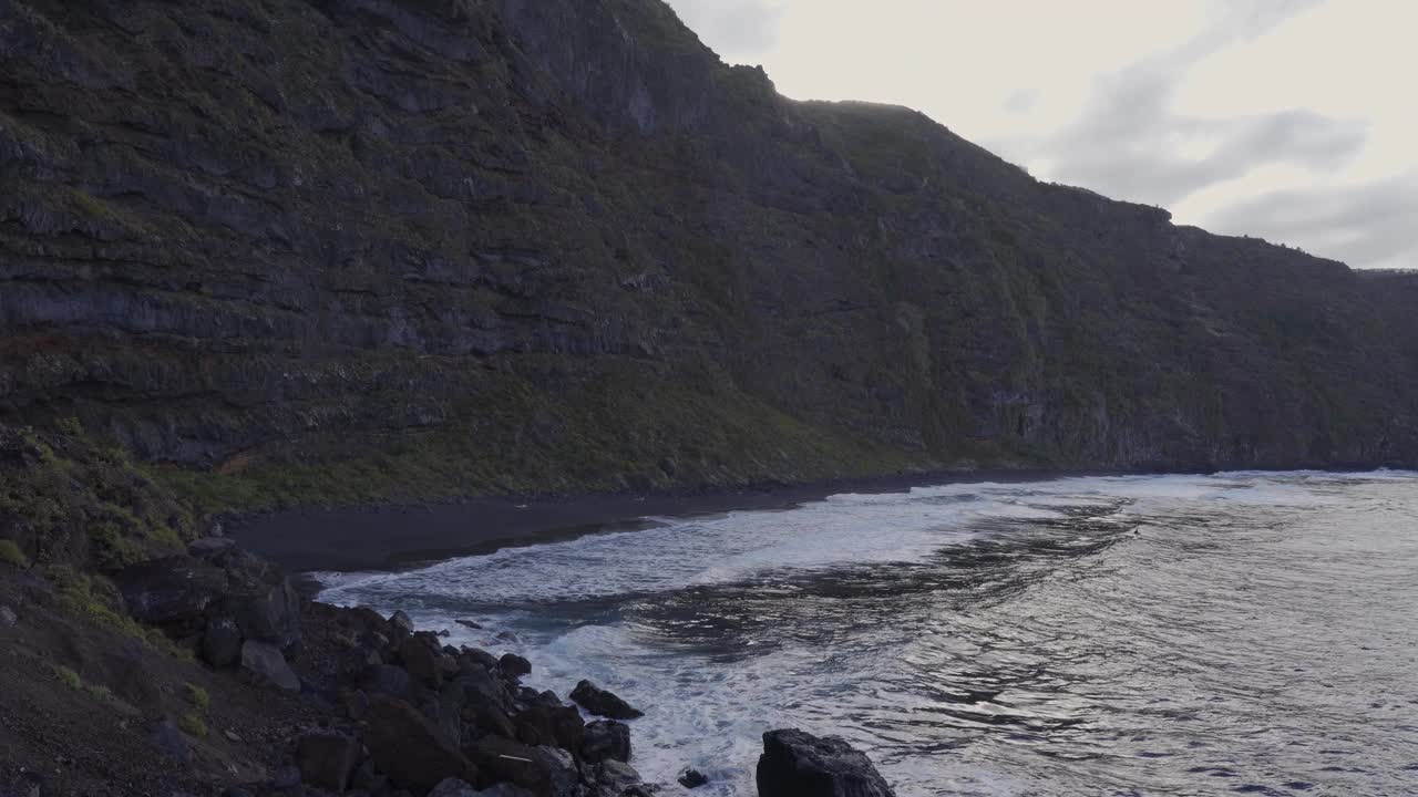 海浪到达一个孤立的海滩与火山黑色的沙子视频素材