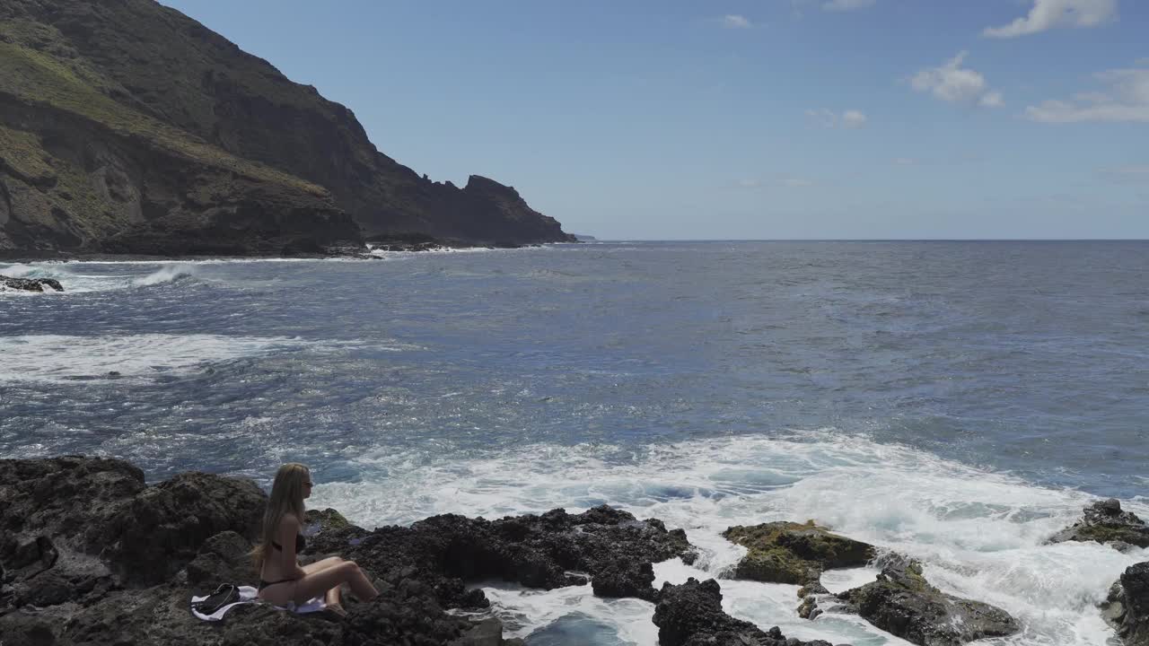 女人坐在岩石上凝视着溅起的浪花视频素材