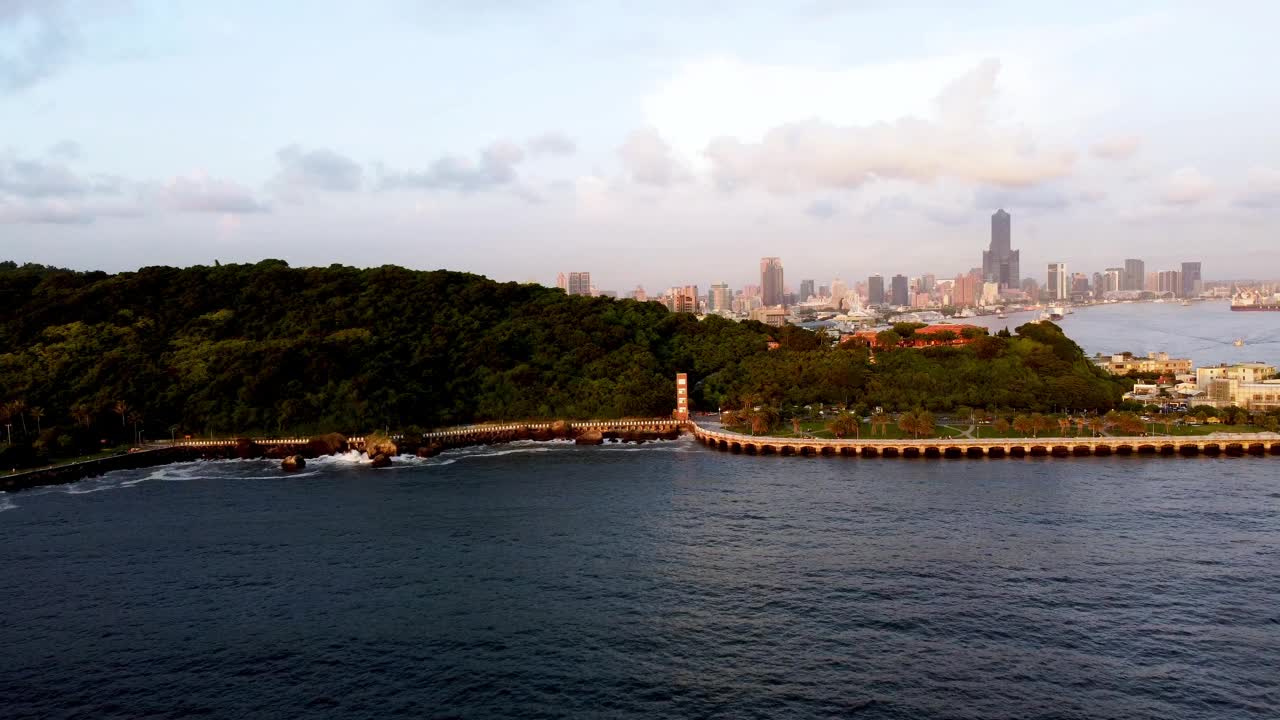 夕阳照耀着城市的天际线和森林覆盖的海岸线，鸟瞰海景，光线温暖视频素材