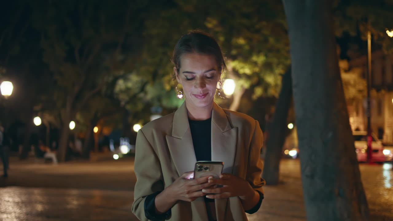 城市女孩在夜晚的街上打电话。面带微笑的迷人女人走在广场上视频素材