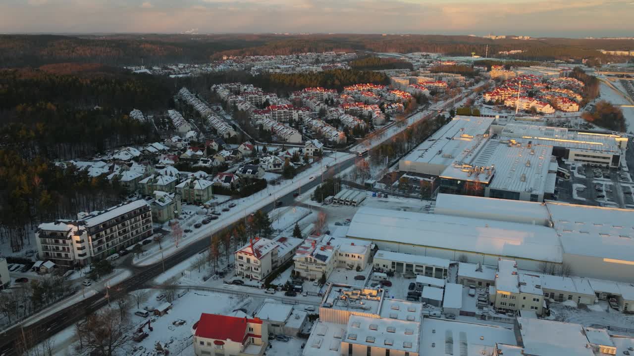 格丁尼亚市郊区冬季下雪。夕阳下的波兰社区和白雪覆盖的工厂建筑。背景中的森林景观。慢速前进无人机飞行。视频素材