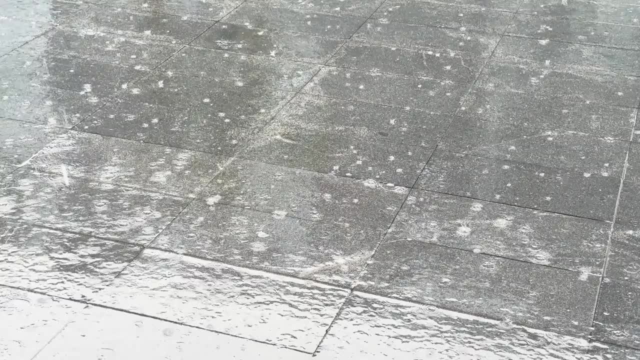 大滴的夏季雨水落在城市的沥青上。雨沿着潮湿的人行道下着毛毛雨。水珠飞溅。人行道上充满了水视频素材