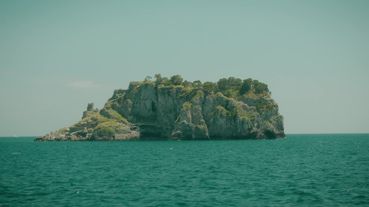 在一个阳光明媚的夏日旅行中，从卡普里岛滨海格兰德镇附近的船上俯瞰崎岖的绿色岛屿岩石。绿松石水的海景。视频素材