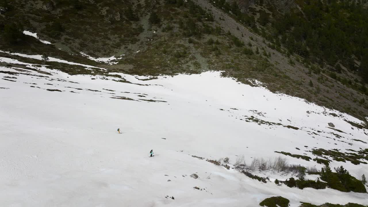 两个滑雪者在草地间的雪地上飞快地滑下峡谷。鸟瞰图视频素材