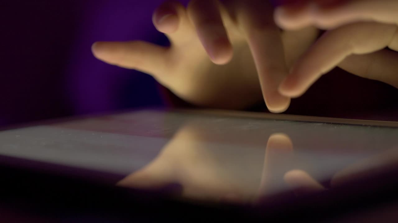 女孩晚上在触摸屏数码平板电脑上打字。在移动电脑上输入文章、文本或文件的人的手近距离。人的手打字文本信息电子邮件在平板电脑触摸屏键盘。视频素材