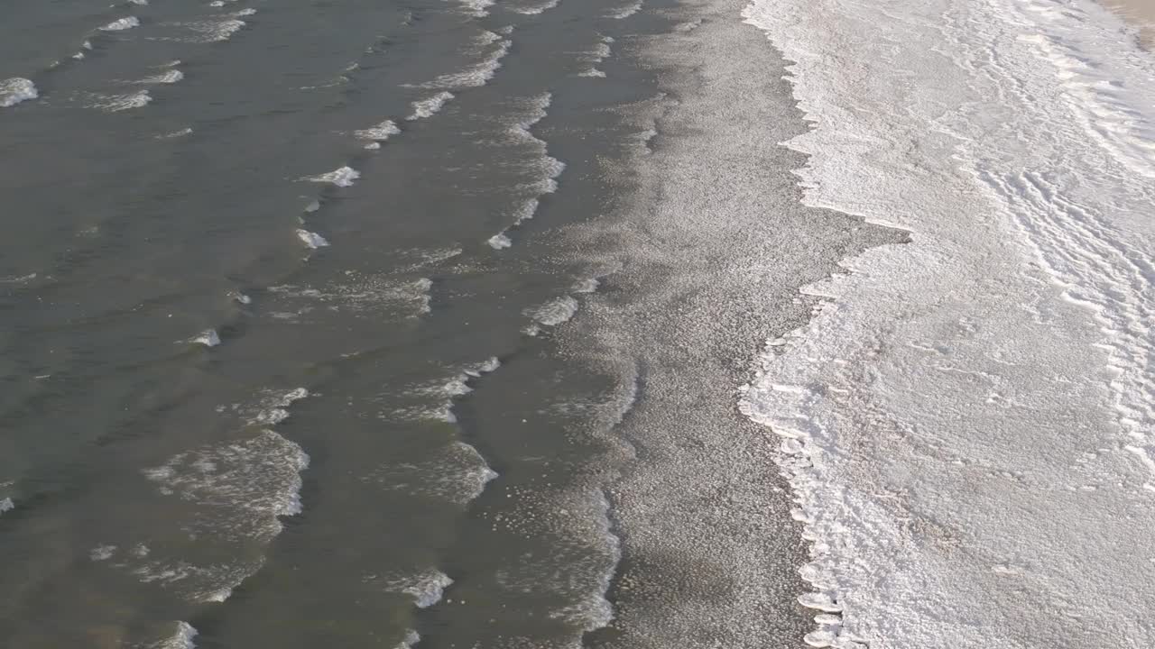 温柔的海浪拍打着沙滩，阳光反射在水面上，鸟瞰视频素材