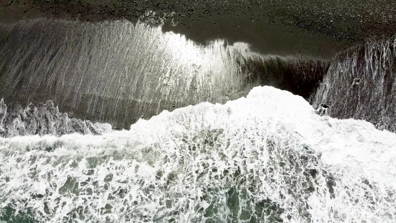 海浪在黑暗的沙滩上破碎，对比泡沫和纹理，鸟瞰图视频素材