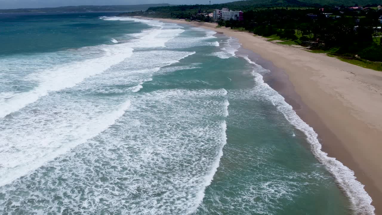 海浪拍打着绿树成荫的沙滩，日光，鸟瞰视频素材