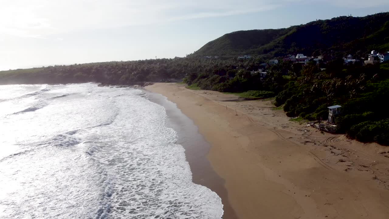 海边的房子俯瞰着宁静的海滩，背景是郁郁葱葱的山丘，金色的阳光视频素材