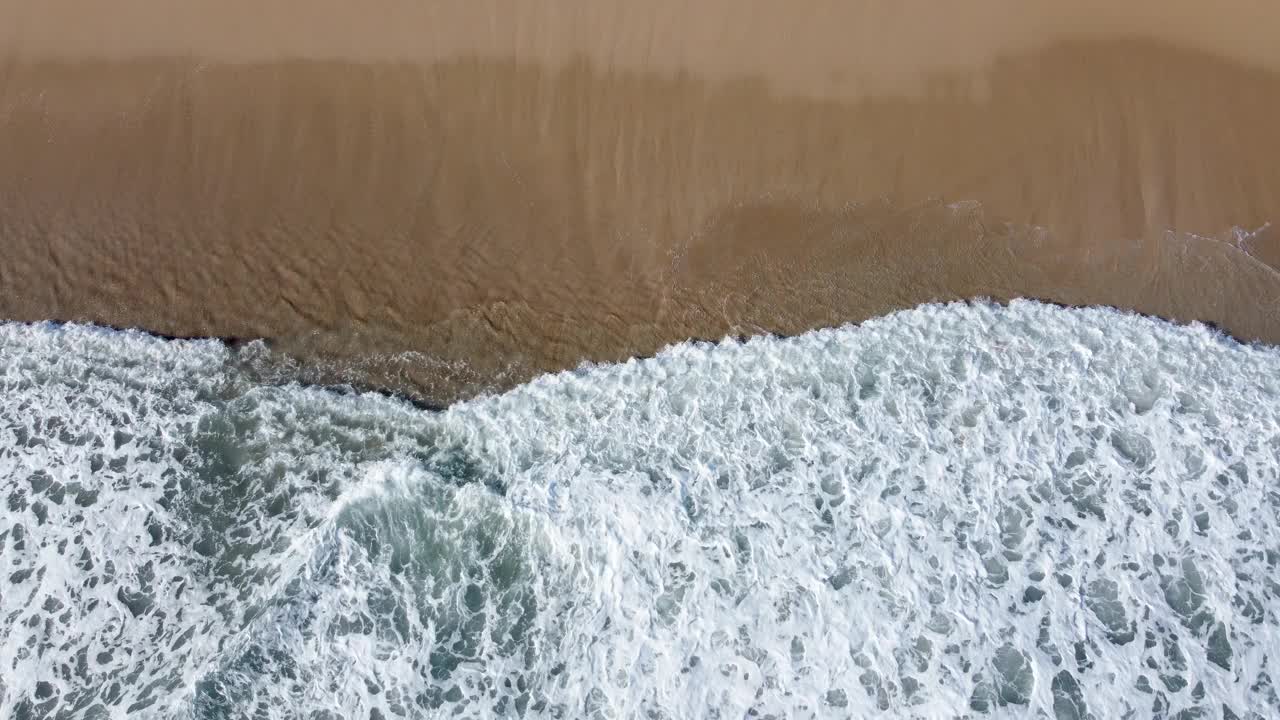 泡沫的海浪冲击着沙滩，从空中俯瞰大自然的原始之美视频素材