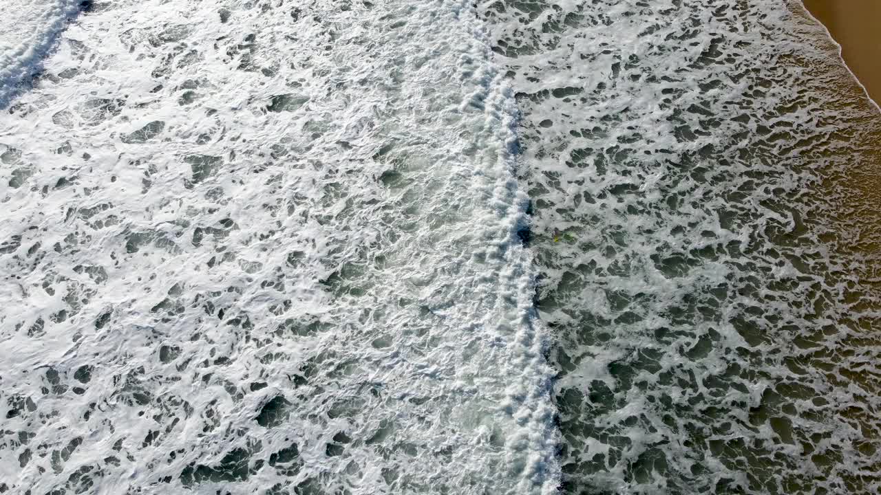 从空中俯瞰，泡沫般的海浪冲刷着沙滩视频素材