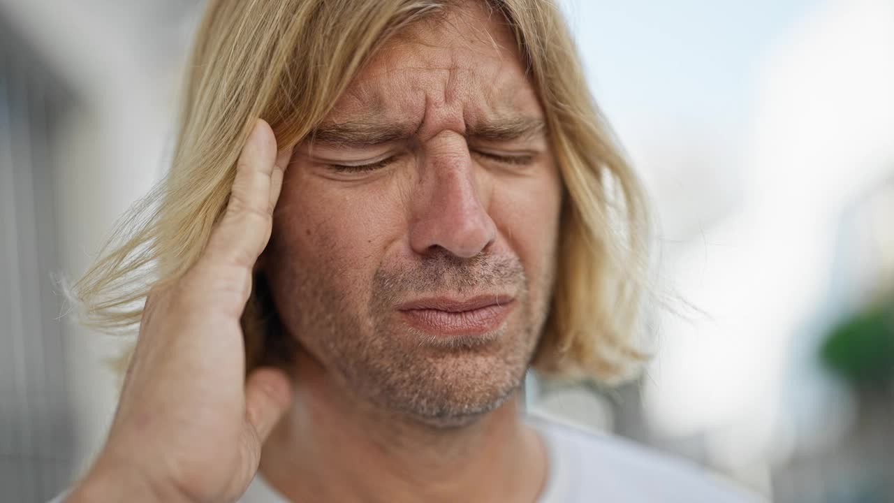 一个痛苦的金发长发的年轻男子在城市的户外昂首挺胸。视频素材