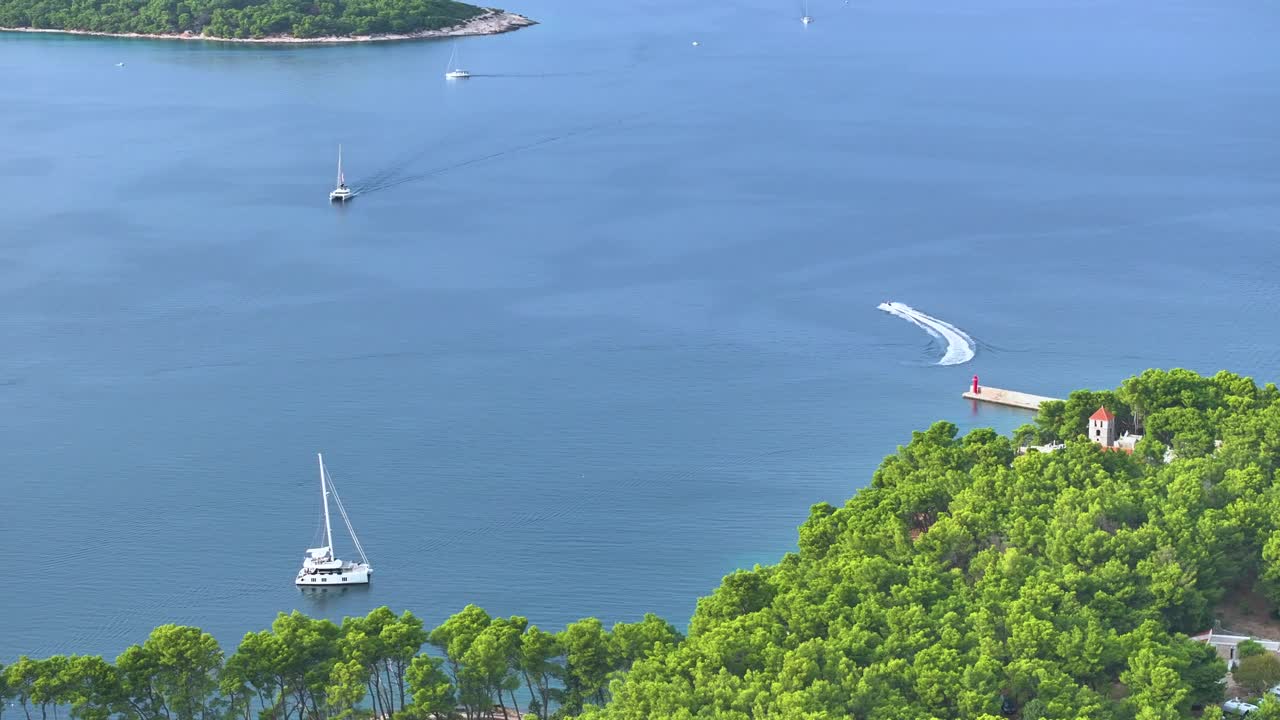 航拍:帆船和水上摩托艇在平静的海面上行驶，周围是郁郁葱葱的沿海植物视频素材