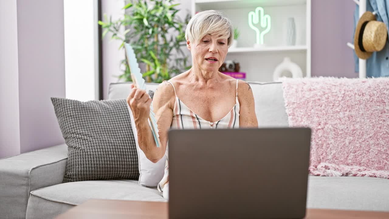 一个成熟的女人在现代的客厅里用风扇给自己降温视频素材