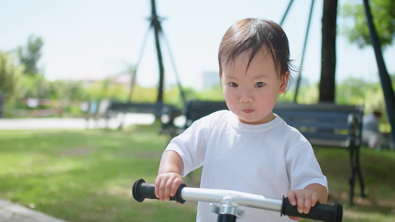 一个小孩在公园里骑自行车。这个孩子穿着一件白衬衫，他的注意力集中在什么东西上。场景是和平和平静的，孩子享受户外活动视频素材