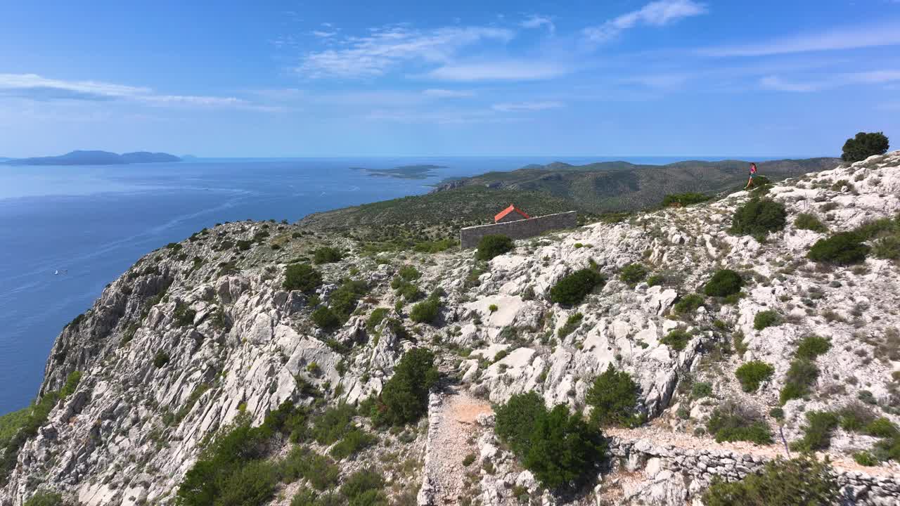 航拍:年轻女子带着她的棕色狗绕着岩石岛徒步旅行。视频素材