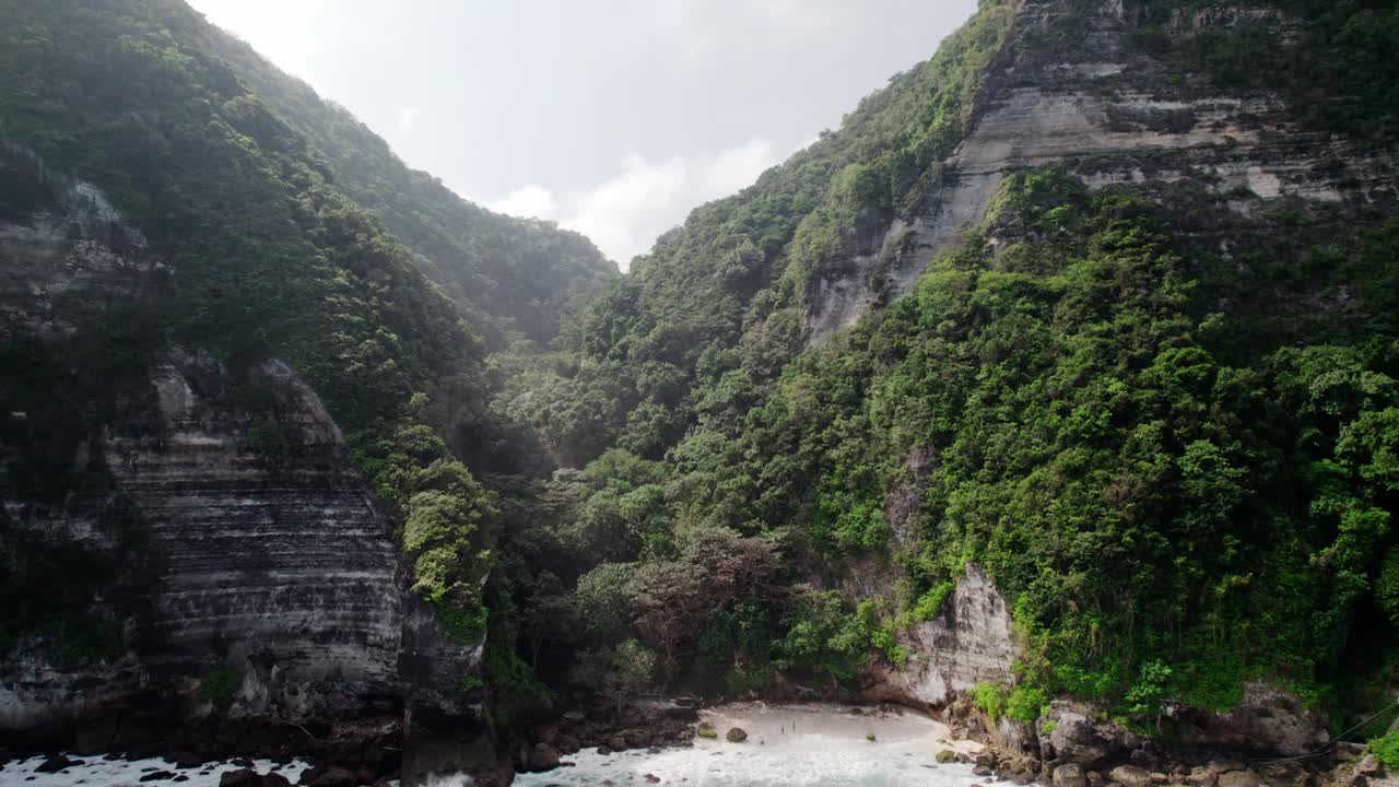 在印度尼西亚巴厘岛的努沙佩尼达，海浪拍打着岩石海岸和石灰岩悬崖。无人机倾斜拍摄视频素材