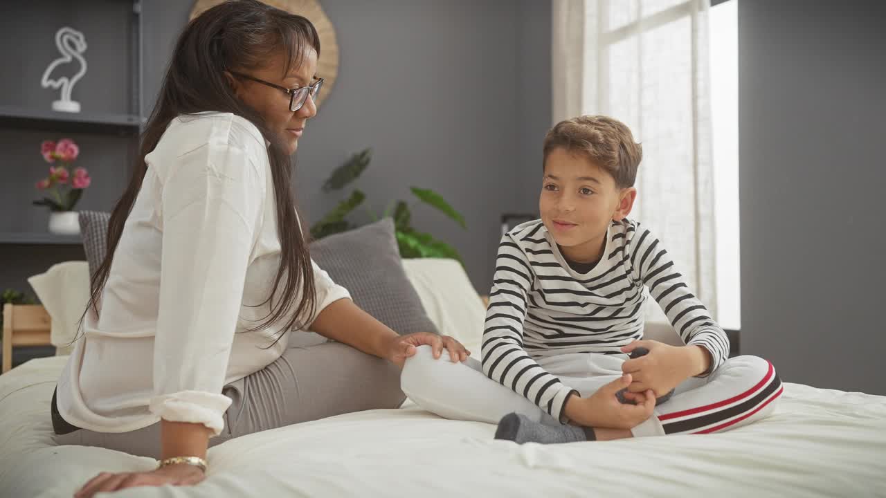 一位慈爱的母亲和她年幼的儿子在舒适的卧室床上分享温柔的时刻，反映了室内的温暖和家庭纽带。视频素材