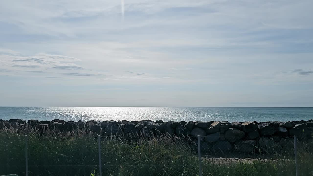 宁静的海滨景观与岩石屏障。宁静的海景，波光粼粼的海水被崎岖的岩石屏障所遮挡。视频素材