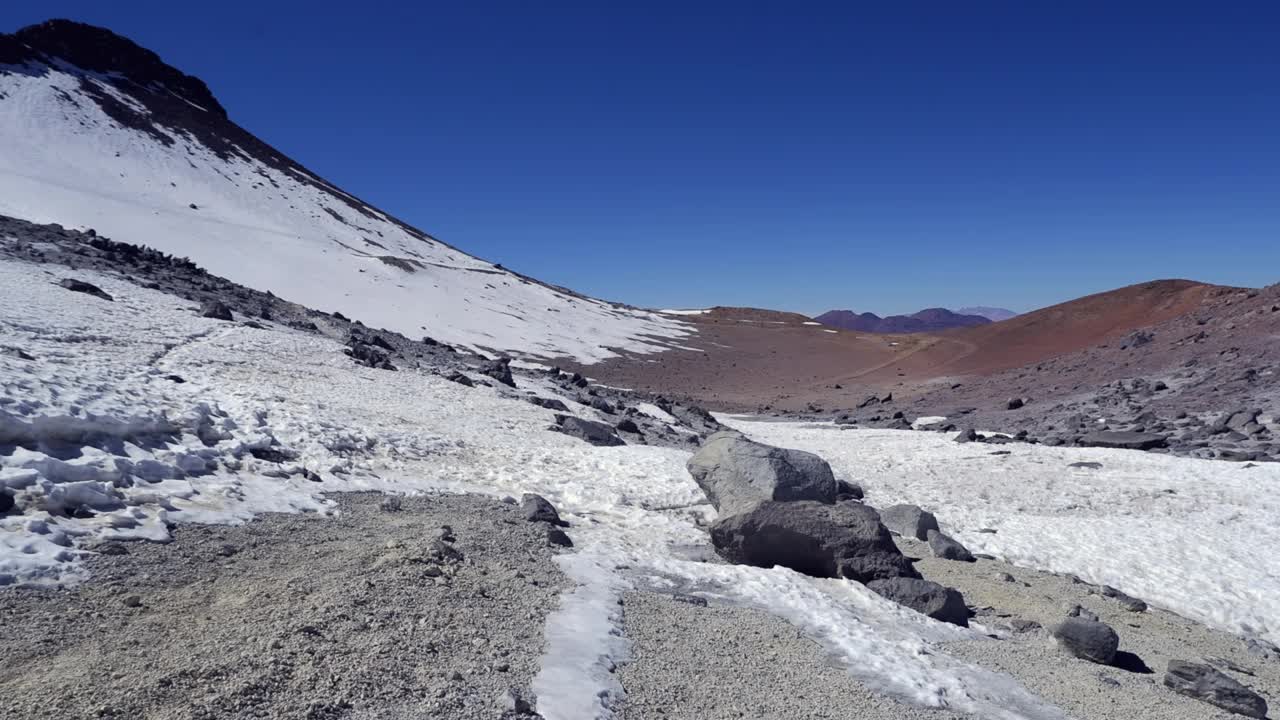 一个孤独的徒步旅行者穿过雪堆向远处的山顶山脊走去视频素材