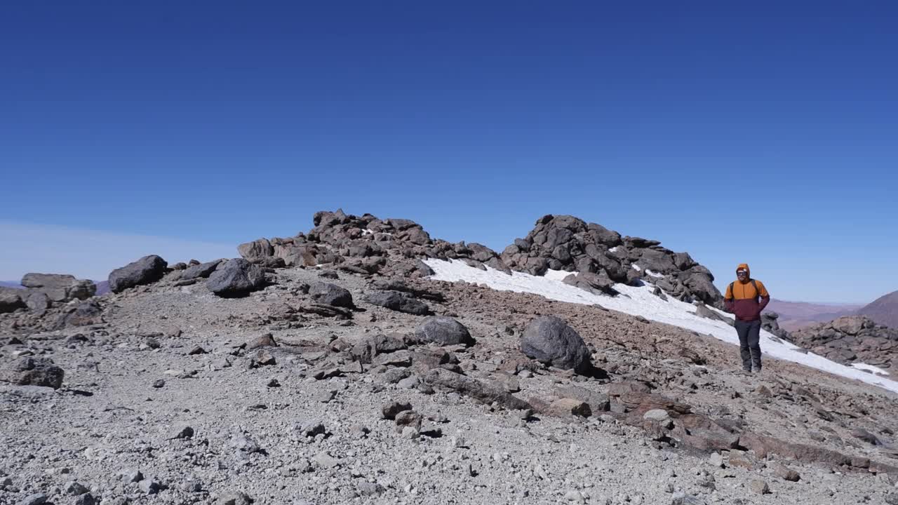 一个人走在山顶的小路上，经过一片雪地，蓝天映衬视频素材