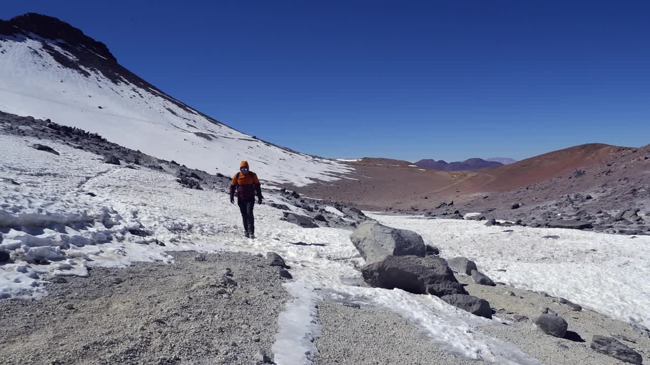 一名男子在凉爽、清爽的一天在智利白雪皑皑的砾石山高原上徒步旅行视频素材