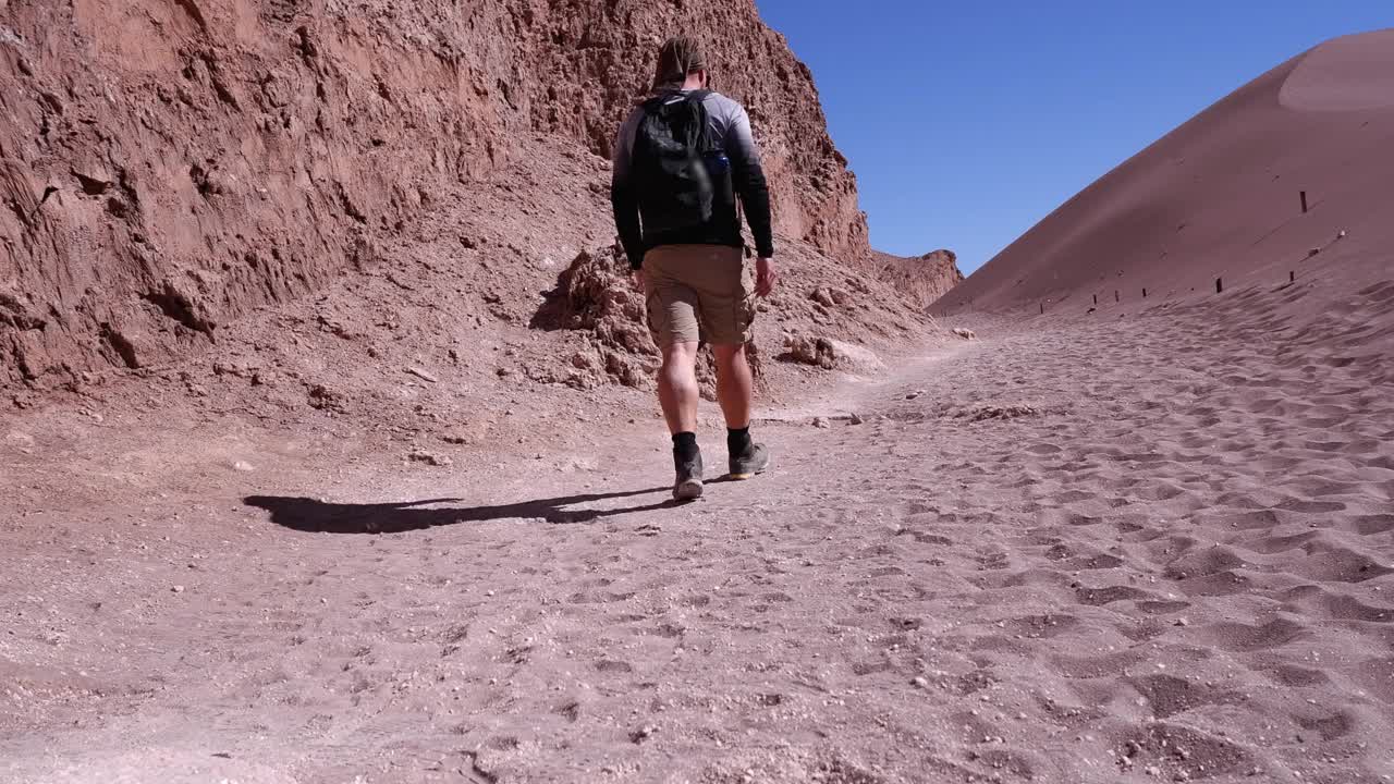 智利阿塔卡马地区，一个人沿着红色的沙漠岩石悬崖徒步旅行视频素材