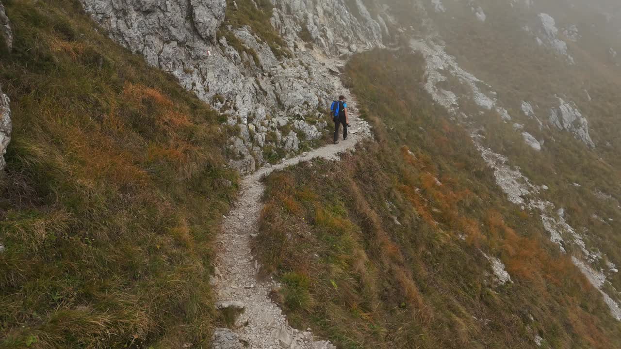 两名徒步旅行者在意大利北部雷塞戈涅山的小路上散步，背景是雾蒙蒙的一天。空中落后视频素材