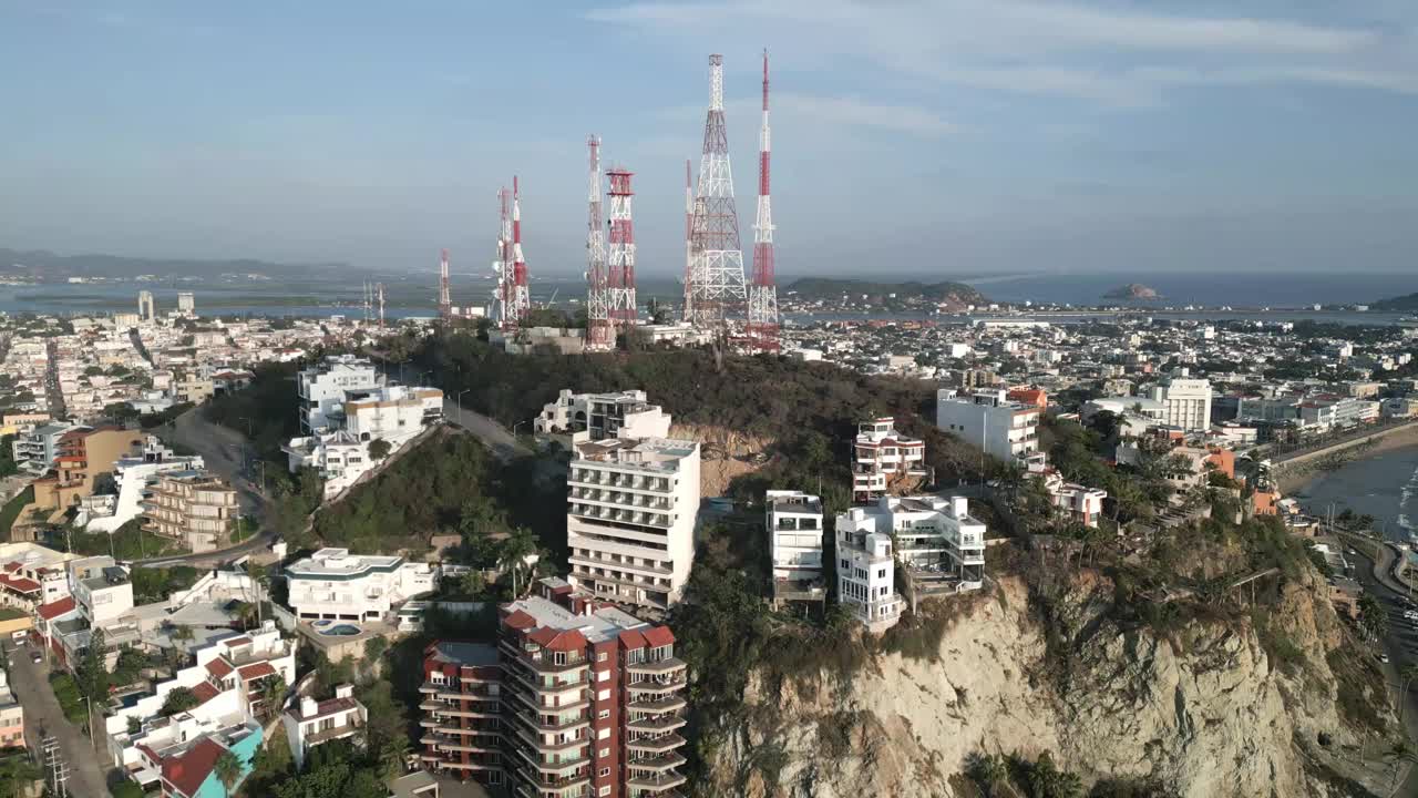 墨西哥马萨特兰太平洋海滩旁边的悬崖上的空中无人机飞行度假村，海浪沿着5G通信塔摧毁了沿海城镇、大海和天际线视频素材